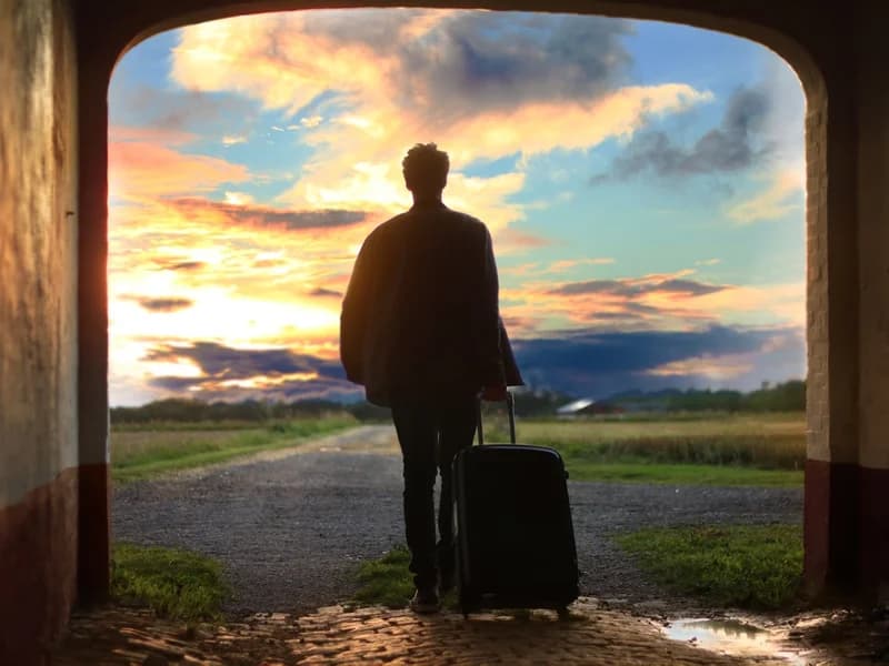 Traveller with a suitcase looking out at a city skyline through an airport window.
