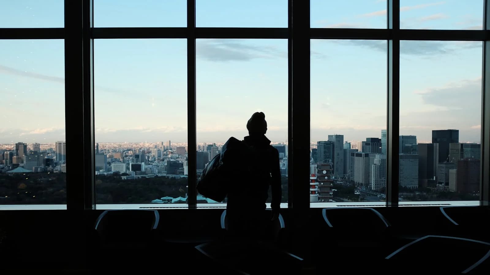 Traveller looking out of an airport window at a city skyline.